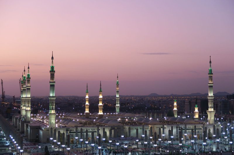 Masjid an-Nabawi in Madinah at twilight, its minarets lit against a pink sky